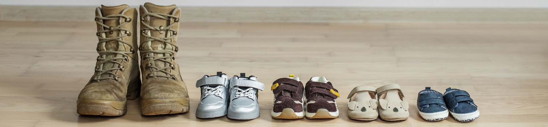 Old worn military boots and lot of baby shoes on wooden floor. Military father and family concept.